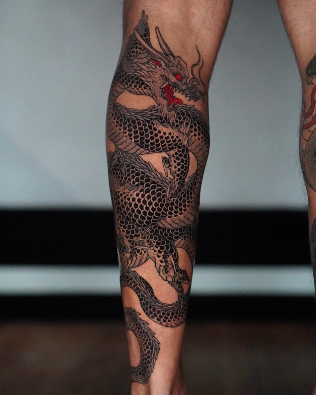 Dragon tattoo with red eyes wrapping around a man's calf and lower leg.
