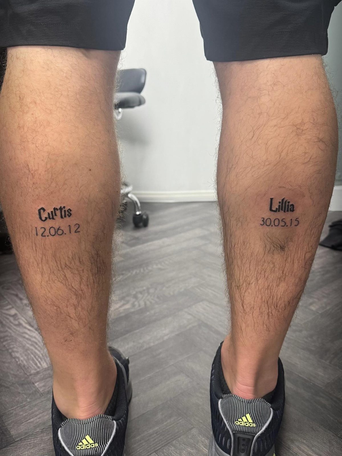 Calf tattoos of the names Curtis and Lillia with corresponding dates in black ink.