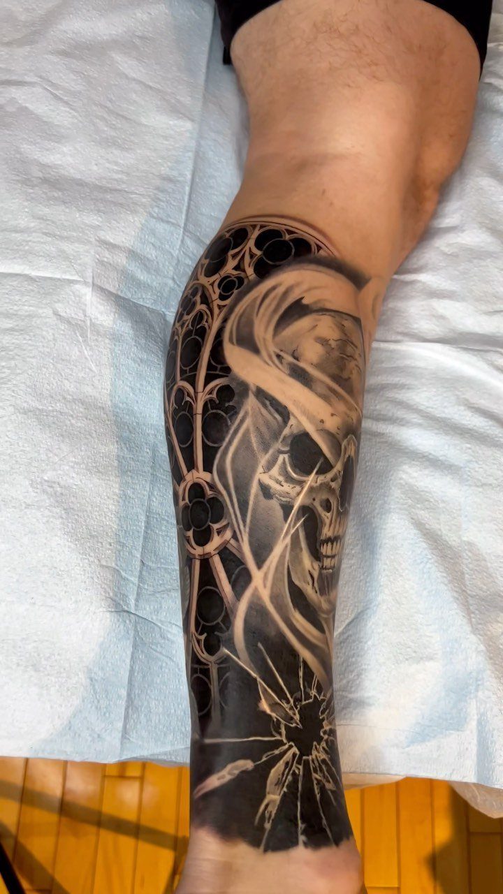 Detailed black and grey skull tattoo with gothic patterns on a man's calf