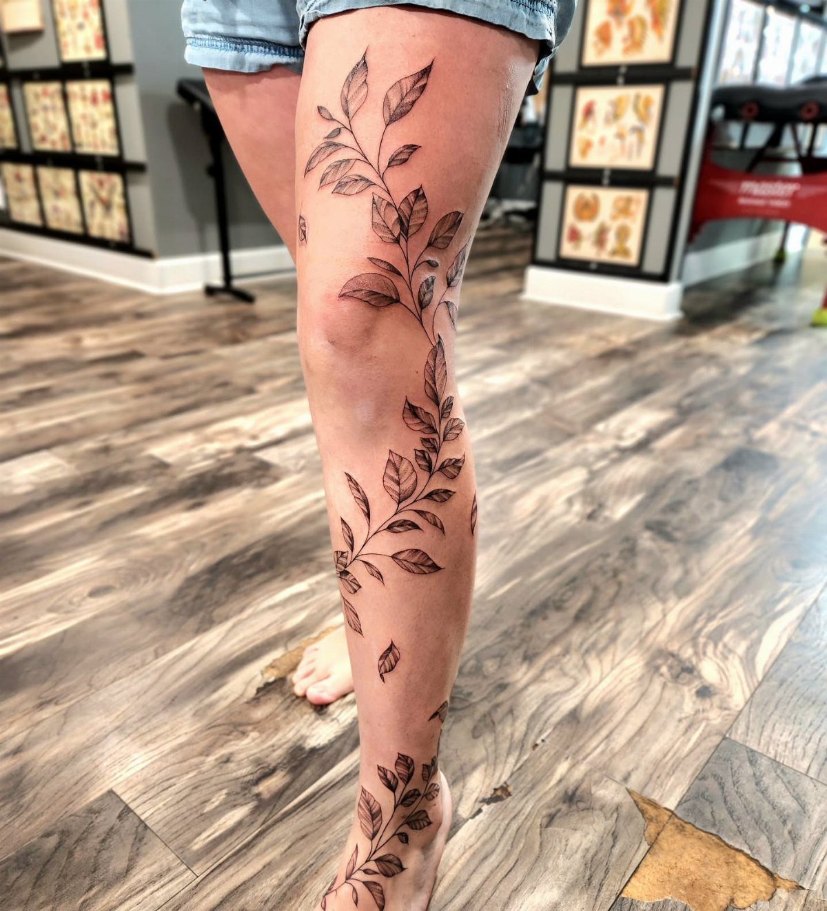 Leafy vine tattoo climbing up a person's leg from ankle to thigh.