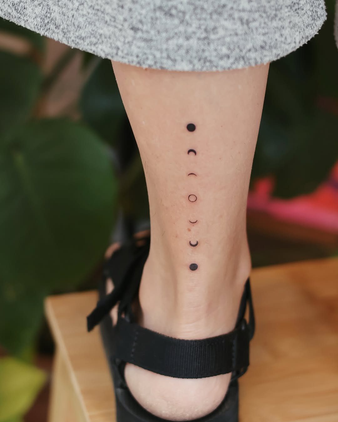 Moon phase tattoos in a vertical line on a person's lower leg and ankle.
