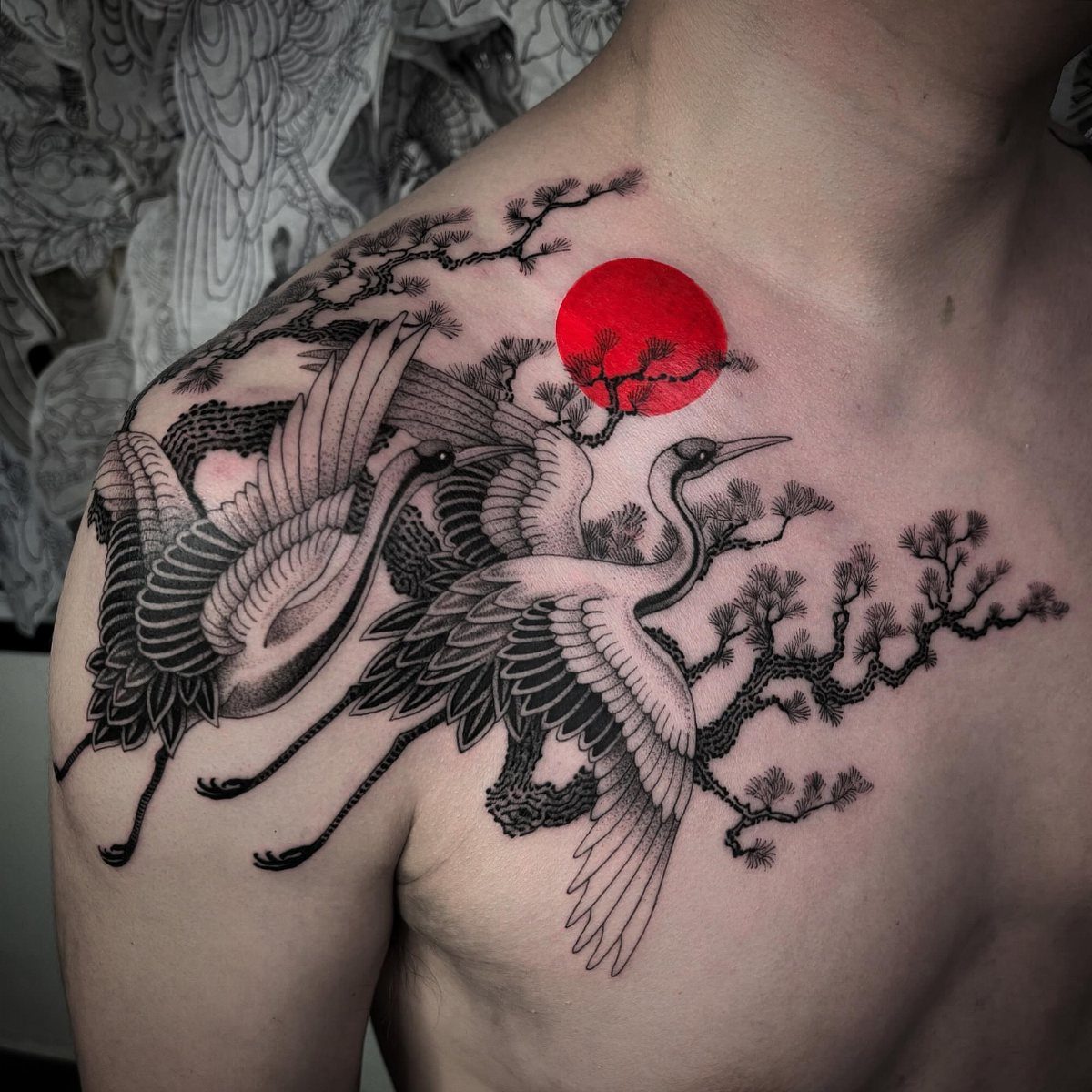 Two cranes and pine branches with a red sun tattooed on a chest.