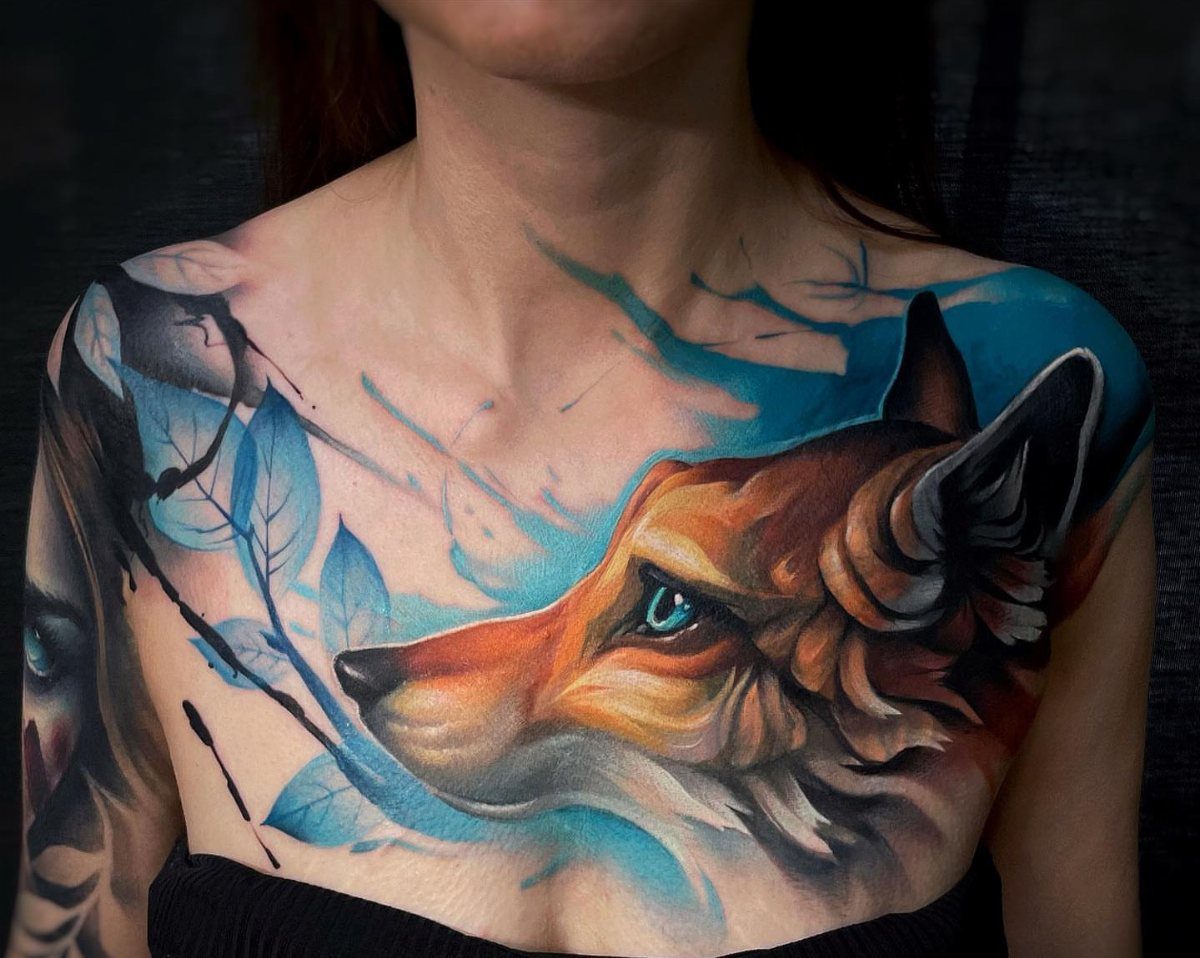 Fox head tattoo on a person's chest with blue artistic accents and leaves.