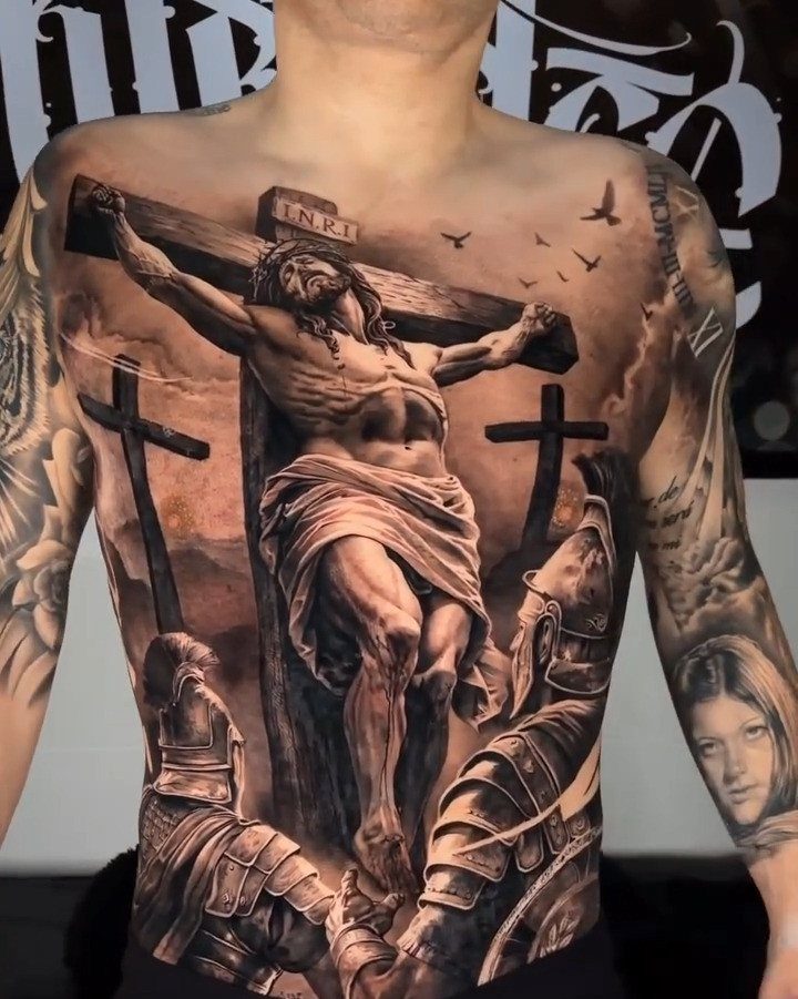 Detailed black and grey torso tattoo depicting Jesus on the cross with Roman soldiers.