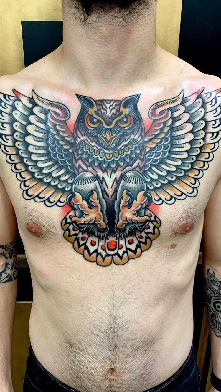 Large owl tattoo with spread wings covering a man's chest in bold colors.