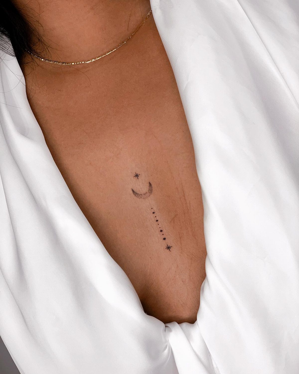 Small crescent moon and stars tattoo on a person's upper chest area.