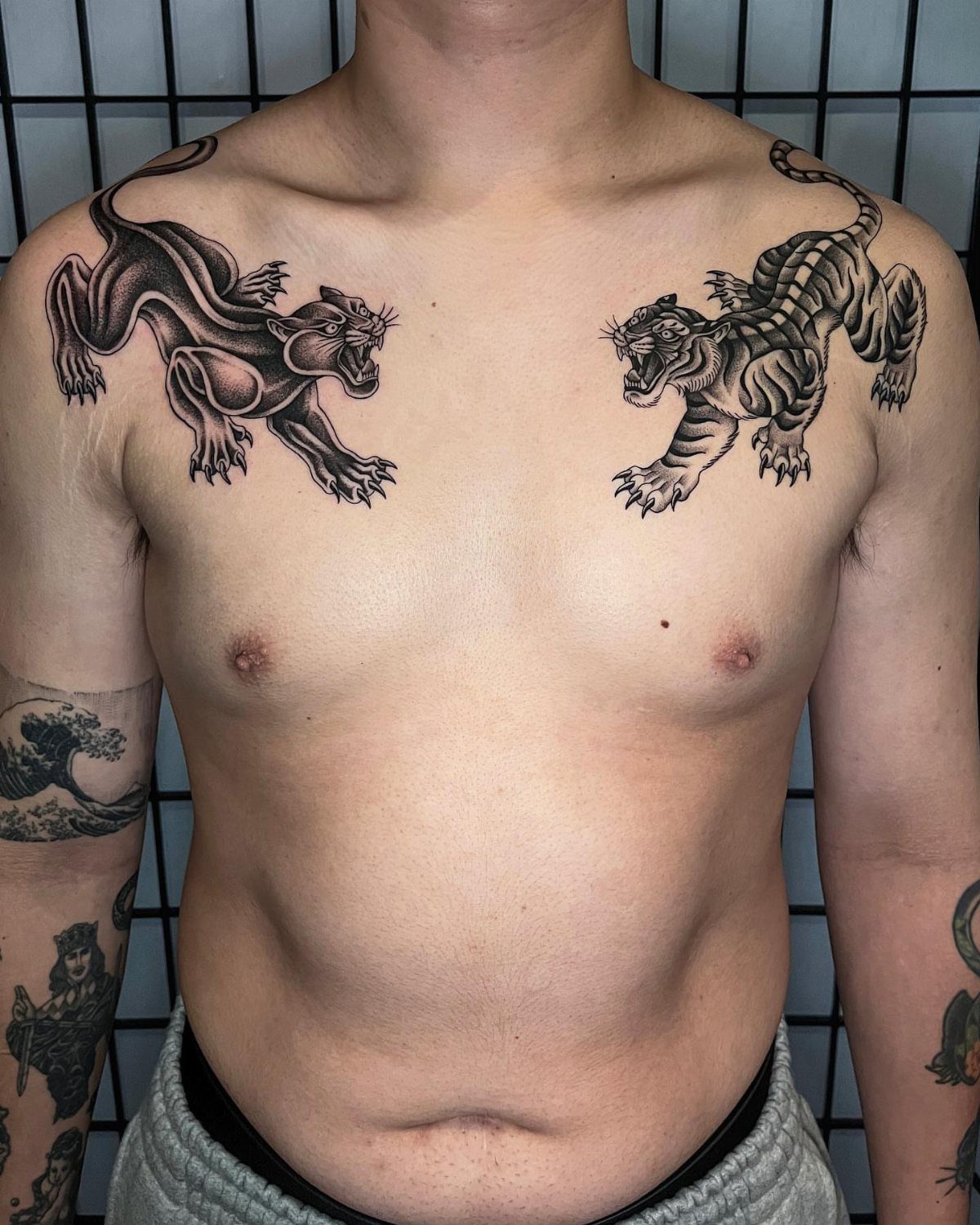 Tiger and panther tattoos on a man's upper chest and shoulders.