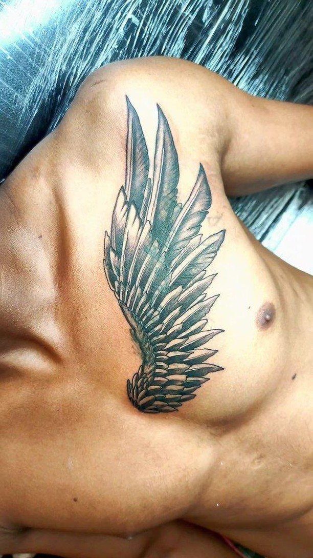 Detailed black and grey wing tattoo on a man's upper chest and pectoral muscle.