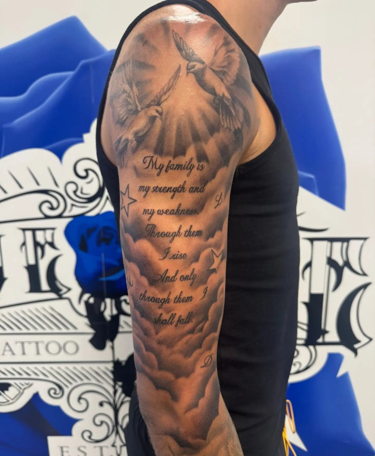Tattoo on a man's arm showing clouds, doves, and script text.