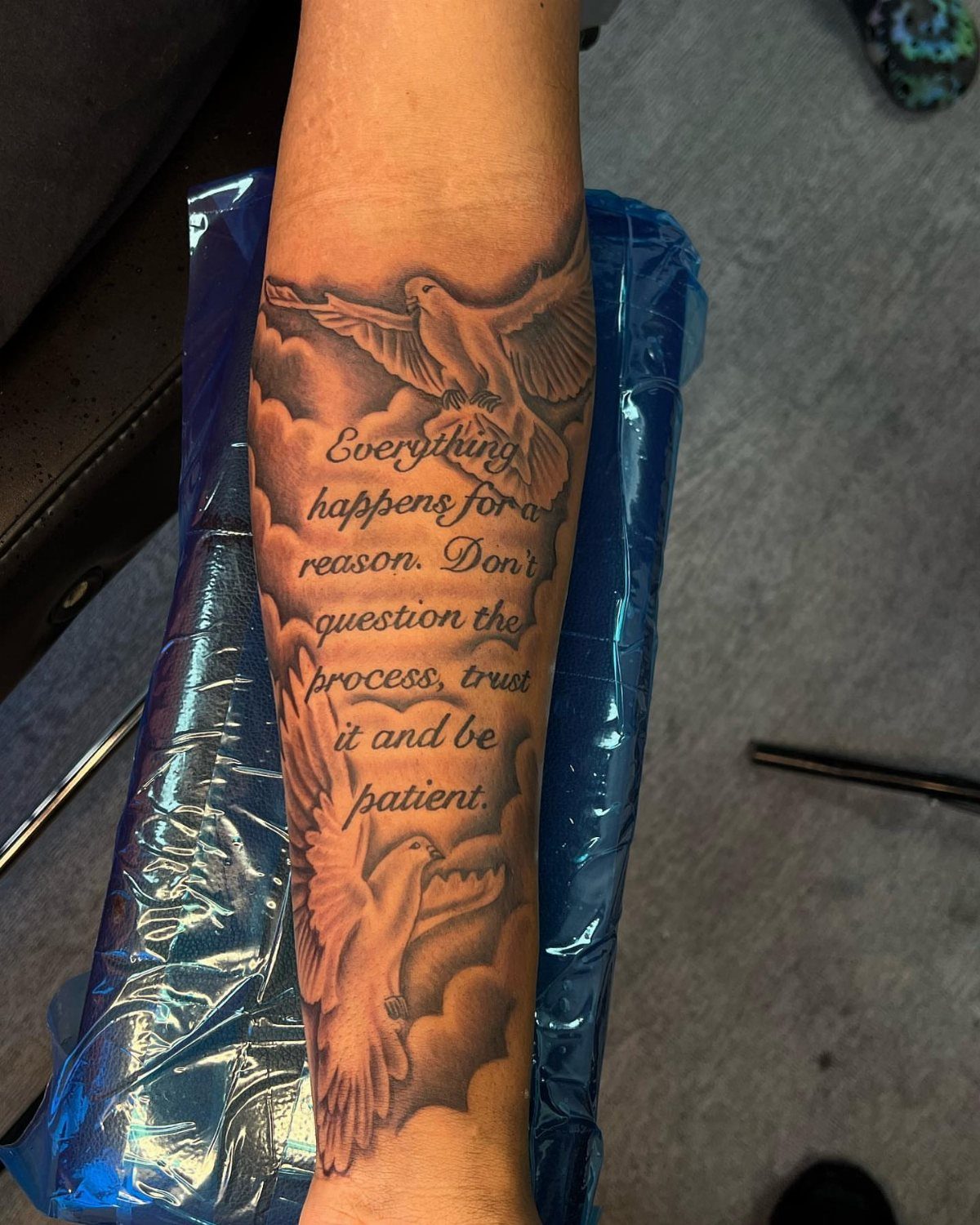 Forearm tattoo of two doves and clouds with a script text quote.