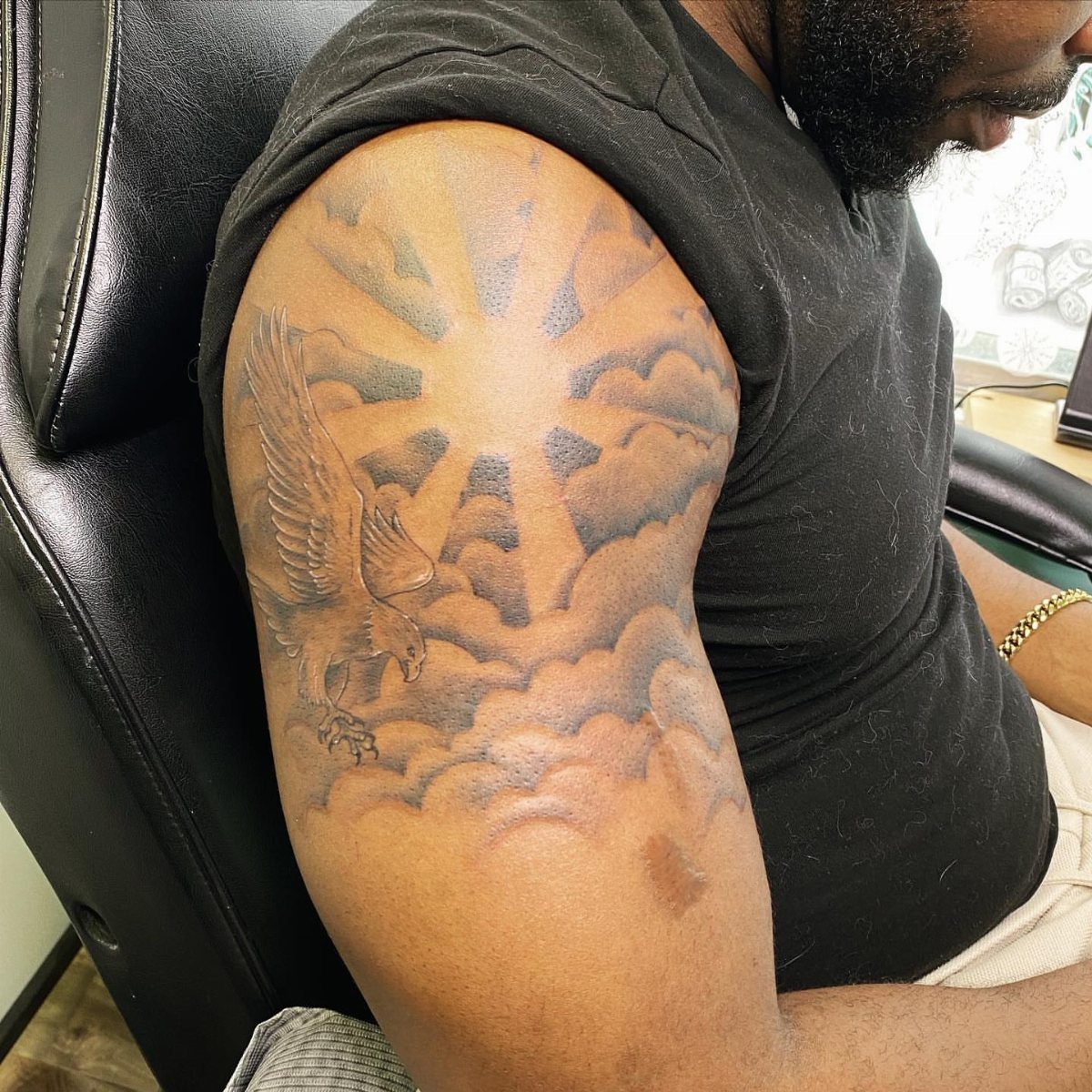 Eagle tattoo on a man's arm flying through clouds with radiating sunbeams