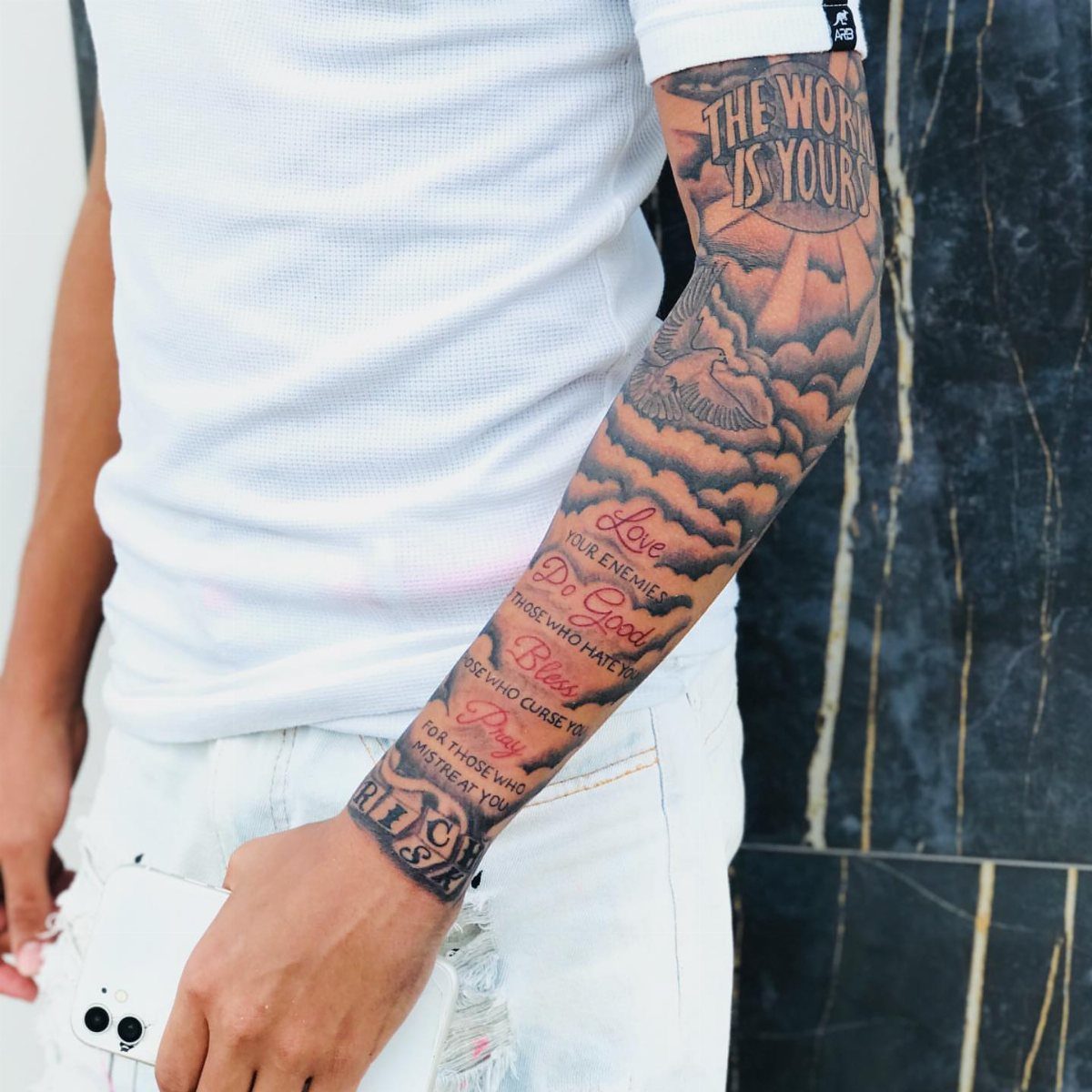 Man's arm with a cloud sleeve tattoo featuring light rays and script text.
