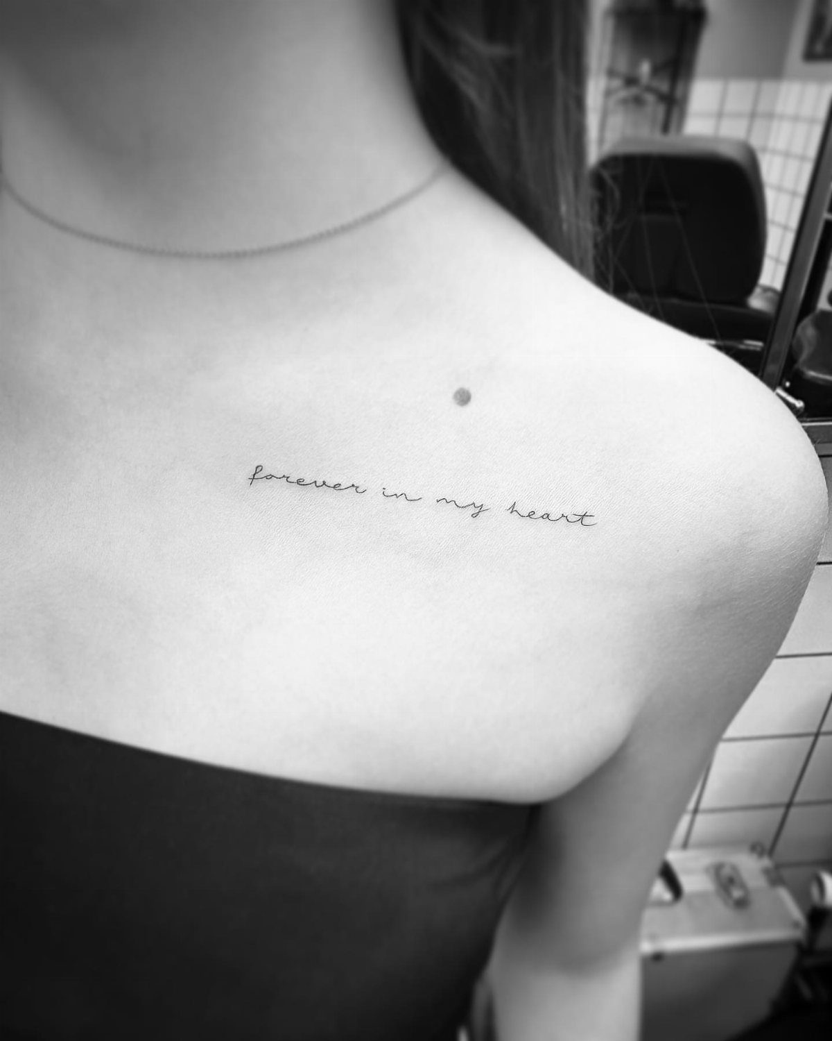 Cursive script tattoo reading forever in my heart on a person's collarbone