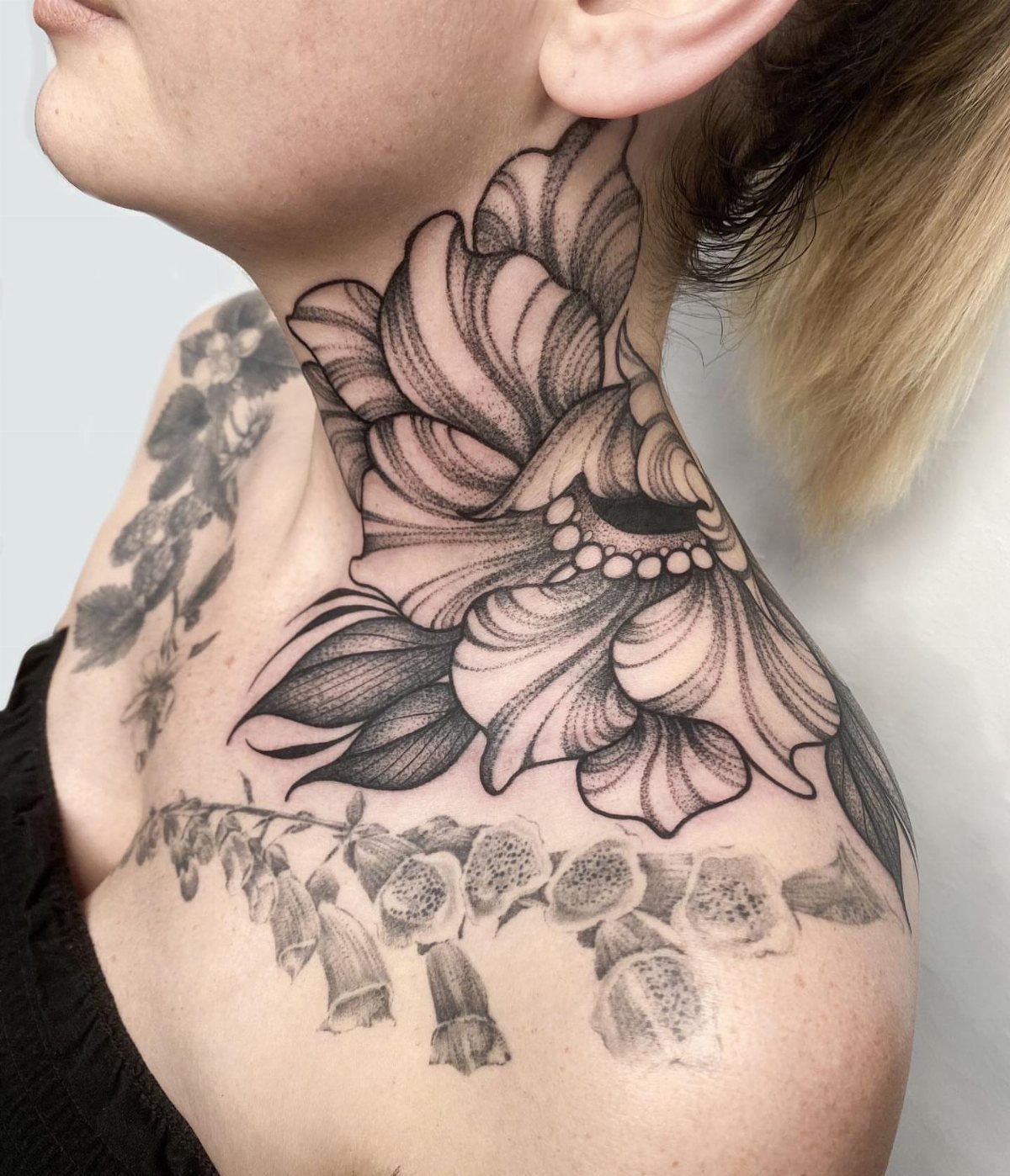 Large black and grey floral tattoos on a person's neck and collarbone area.
