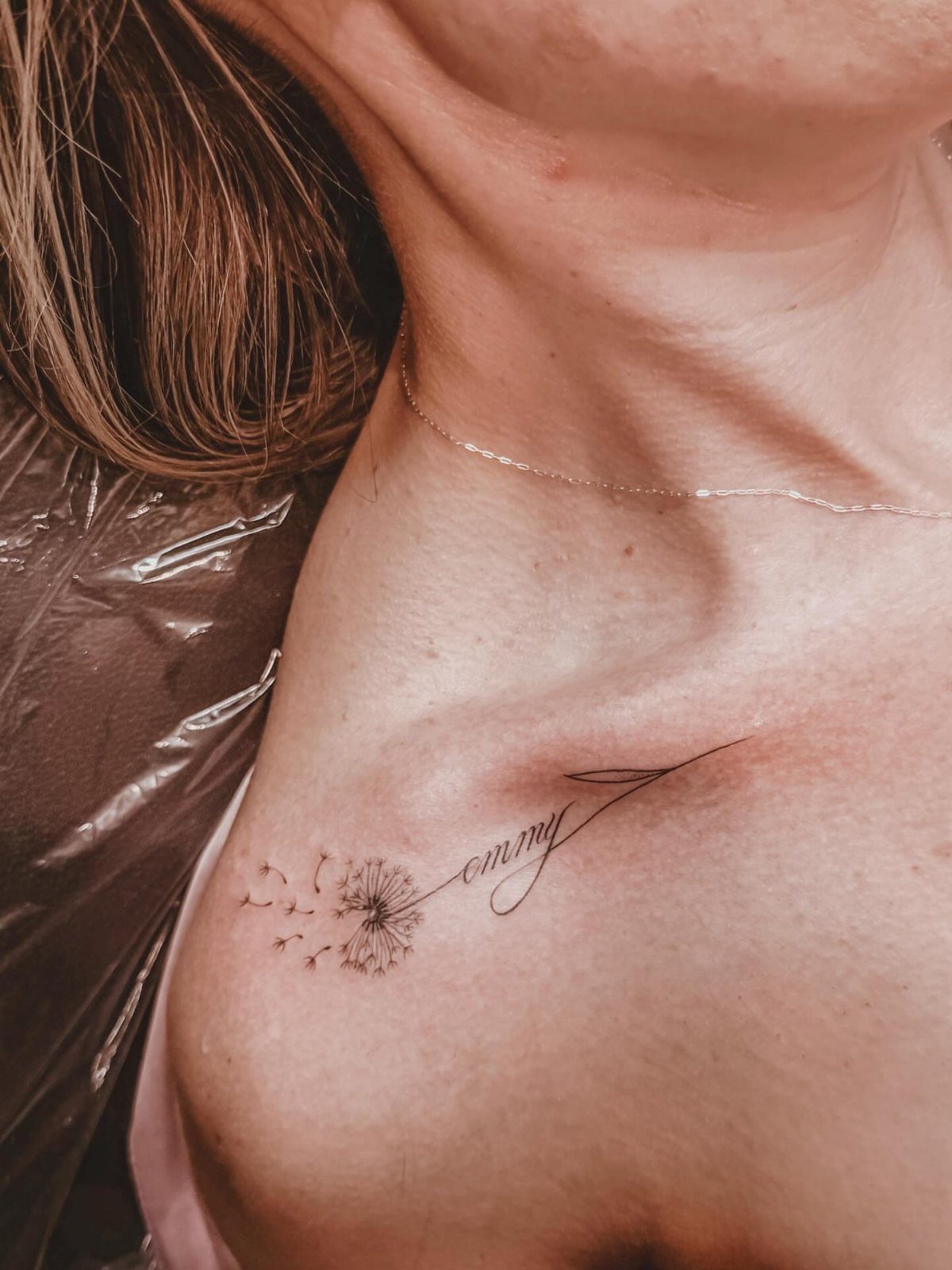Dandelion and cursive script tattoo on a person's collarbone area.