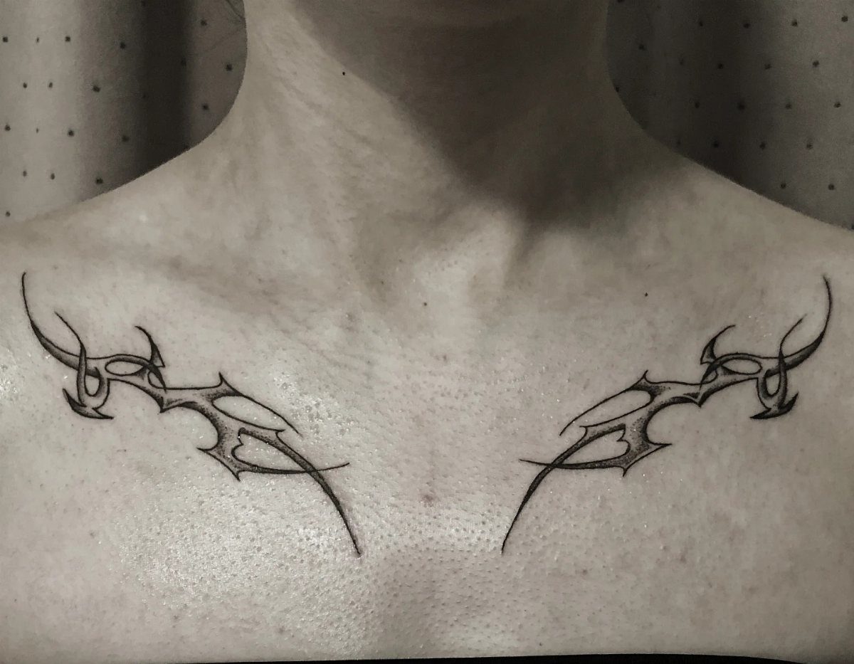 Symmetrical sharp geometric black ink tattoos on a person's collarbone area.