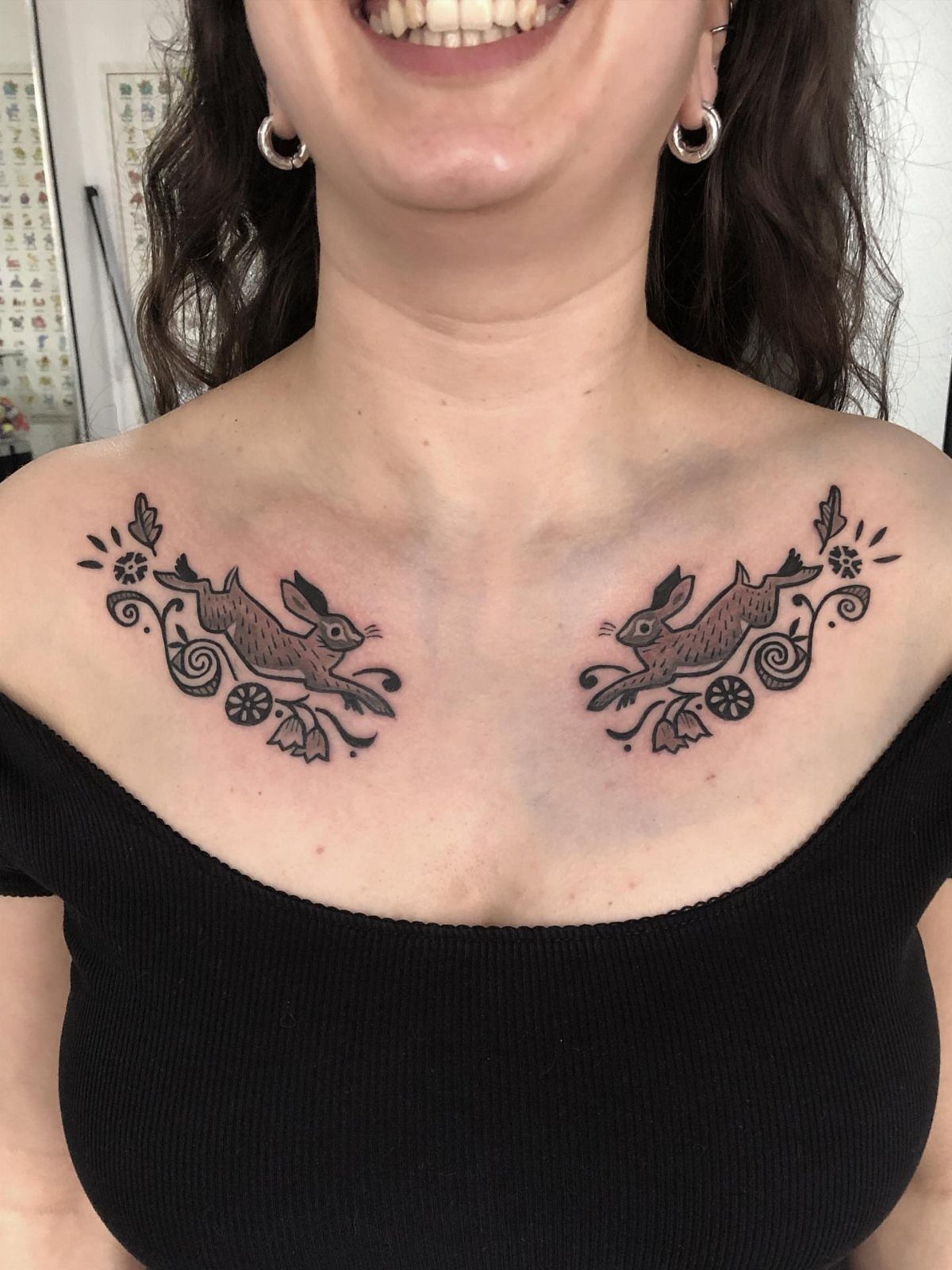 Symmetrical leaping hare tattoos on a person's collarbones with decorative floral accents.