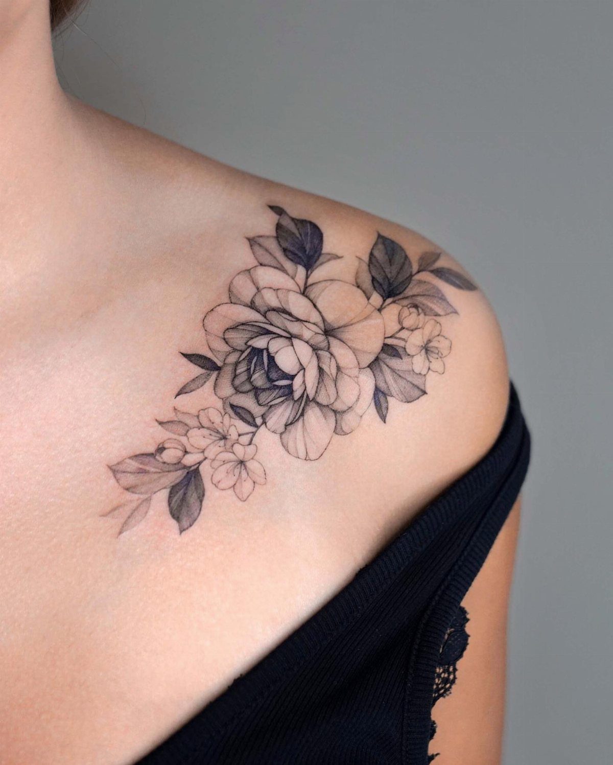 Blooming flower tattoo in black and grey ink on a woman's collarbone and shoulder.