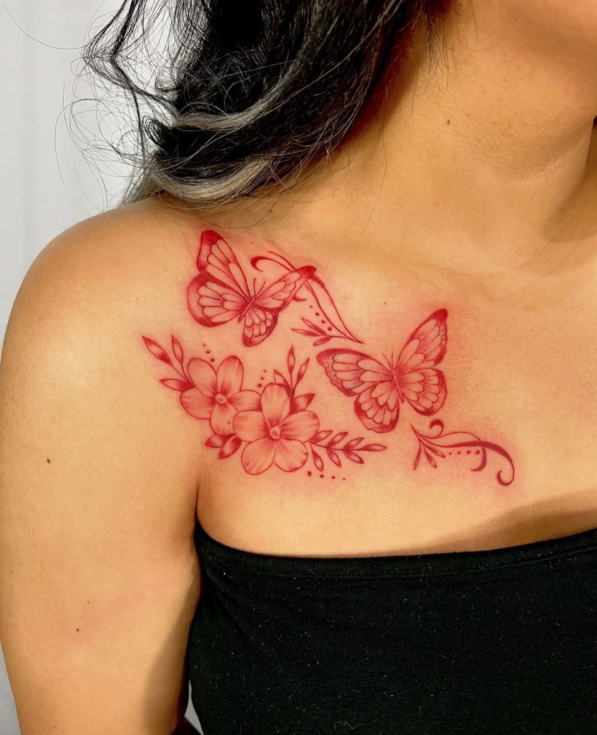 Red ink tattoo of butterflies and blooming flowers on a woman's collarbone.