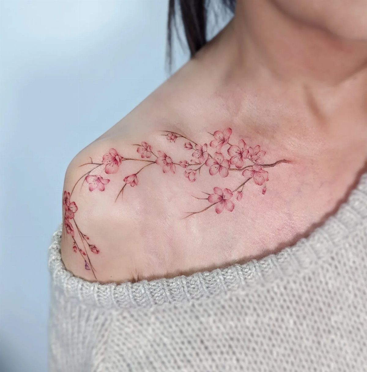 Pink cherry blossom tattoo along a woman's collarbone and shoulder.