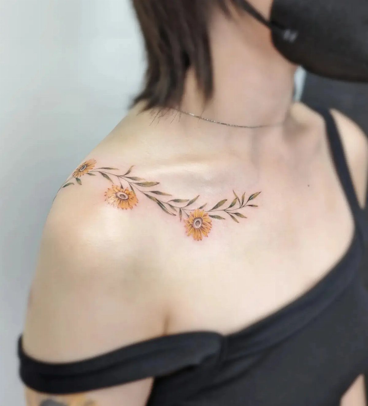Yellow sunflower and leaf tattoo along a woman's collarbone and shoulder.