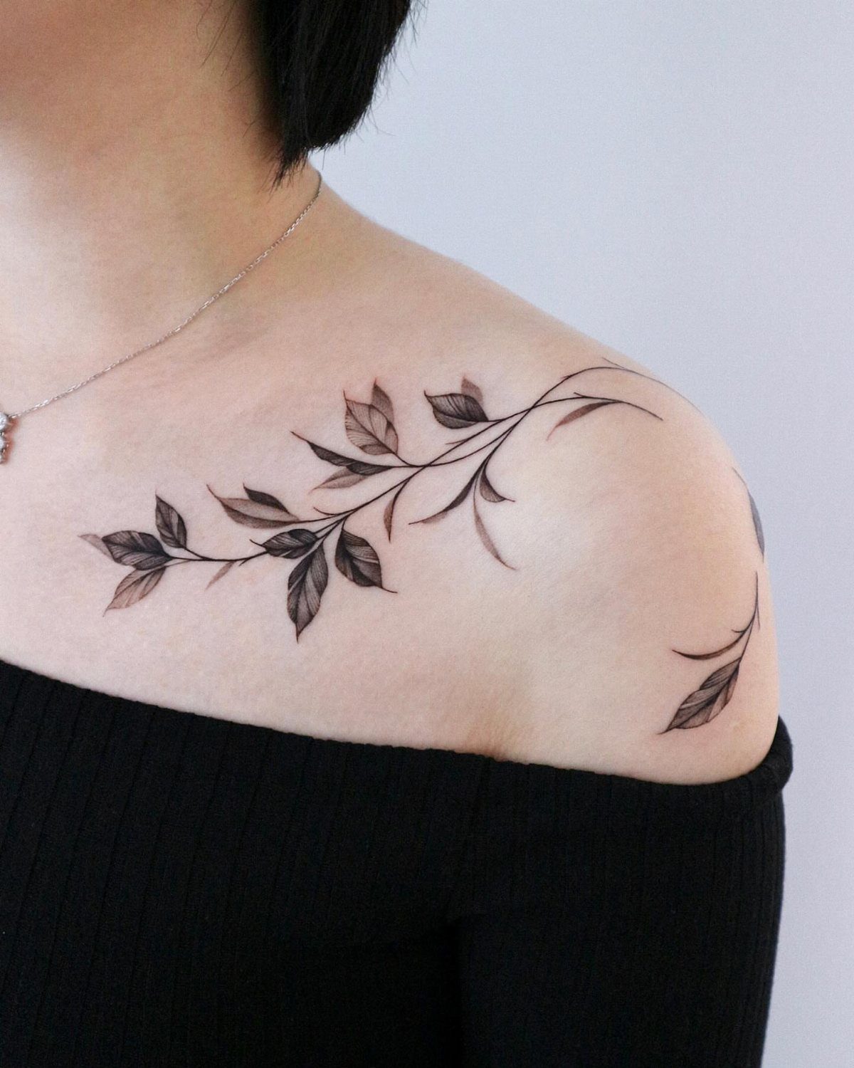 Delicate black ink leafy branch tattoo on a woman's collarbone and shoulder.