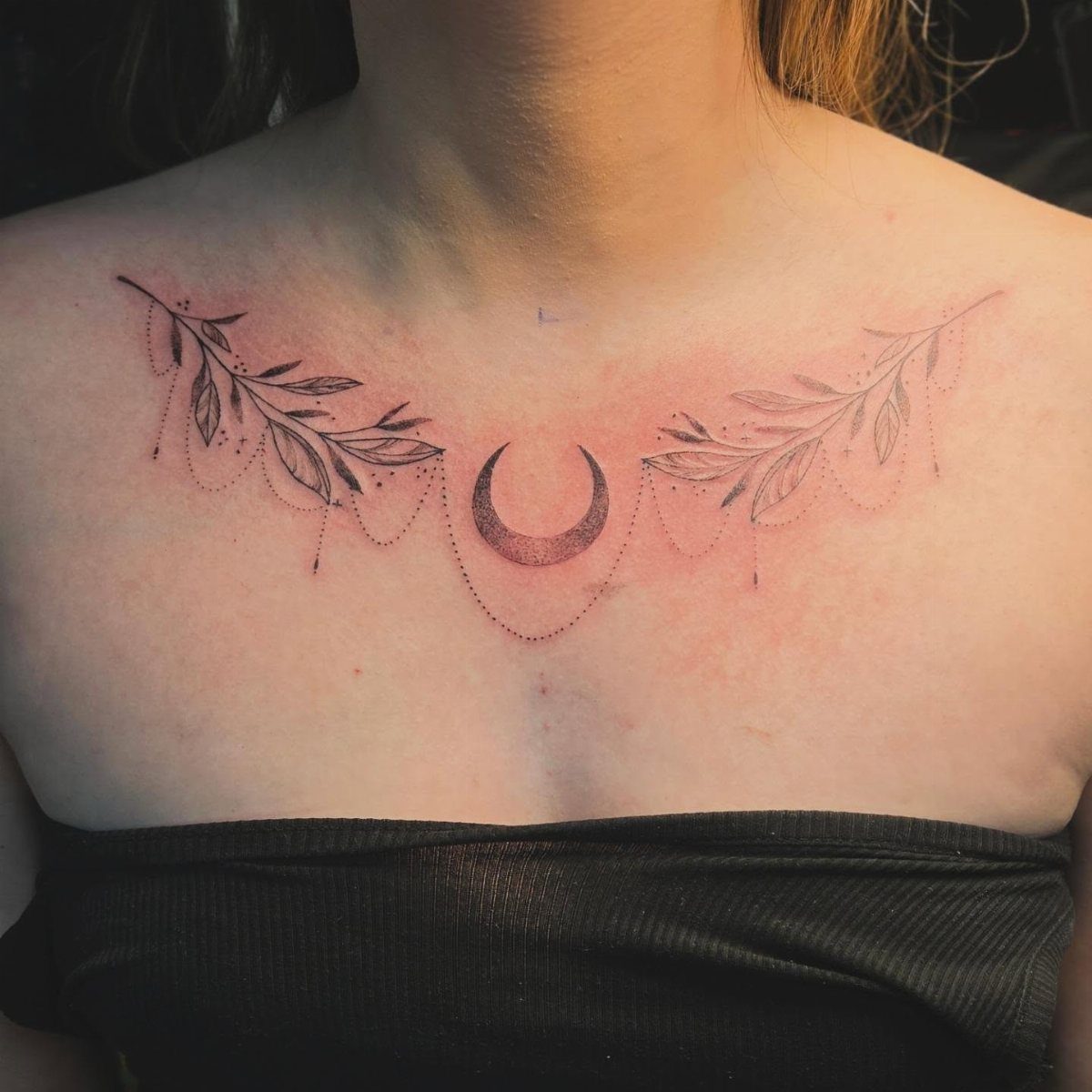 Crescent moon and leafy branch tattoo on a woman's collarbone area