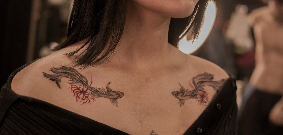 Two matching koi fish tattoos on a woman's collarbones with red accents.