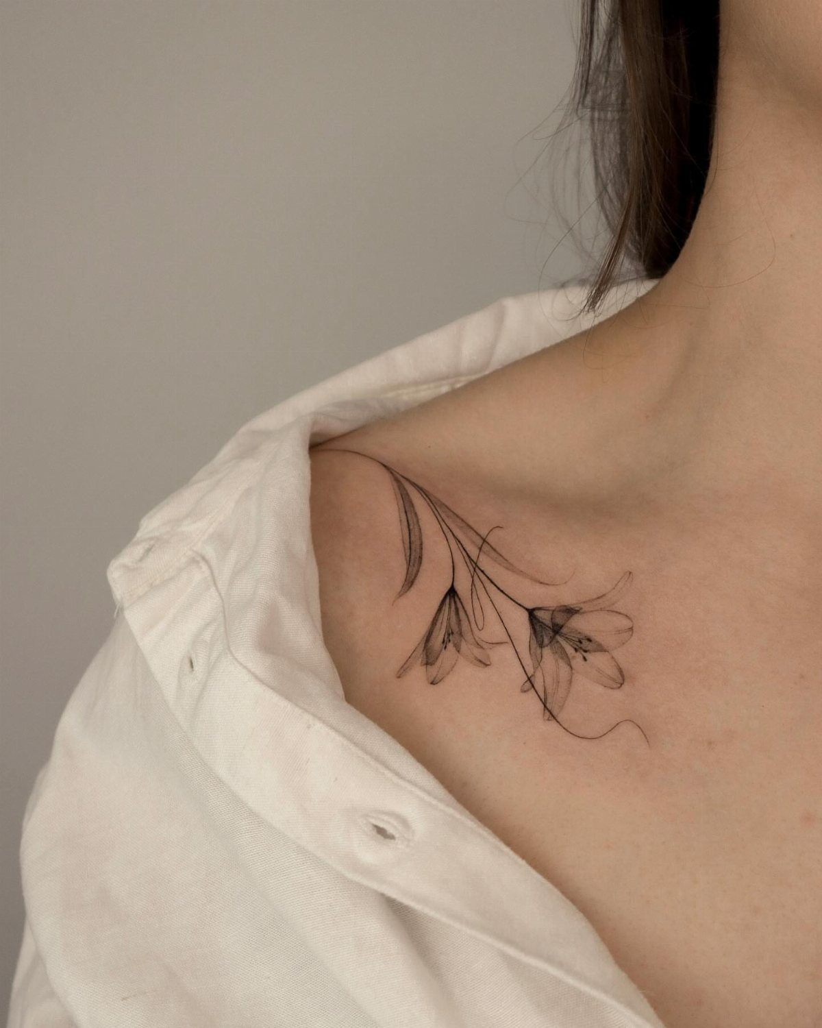 Delicate black ink floral tattoo on a woman's collarbone with a white shirt.