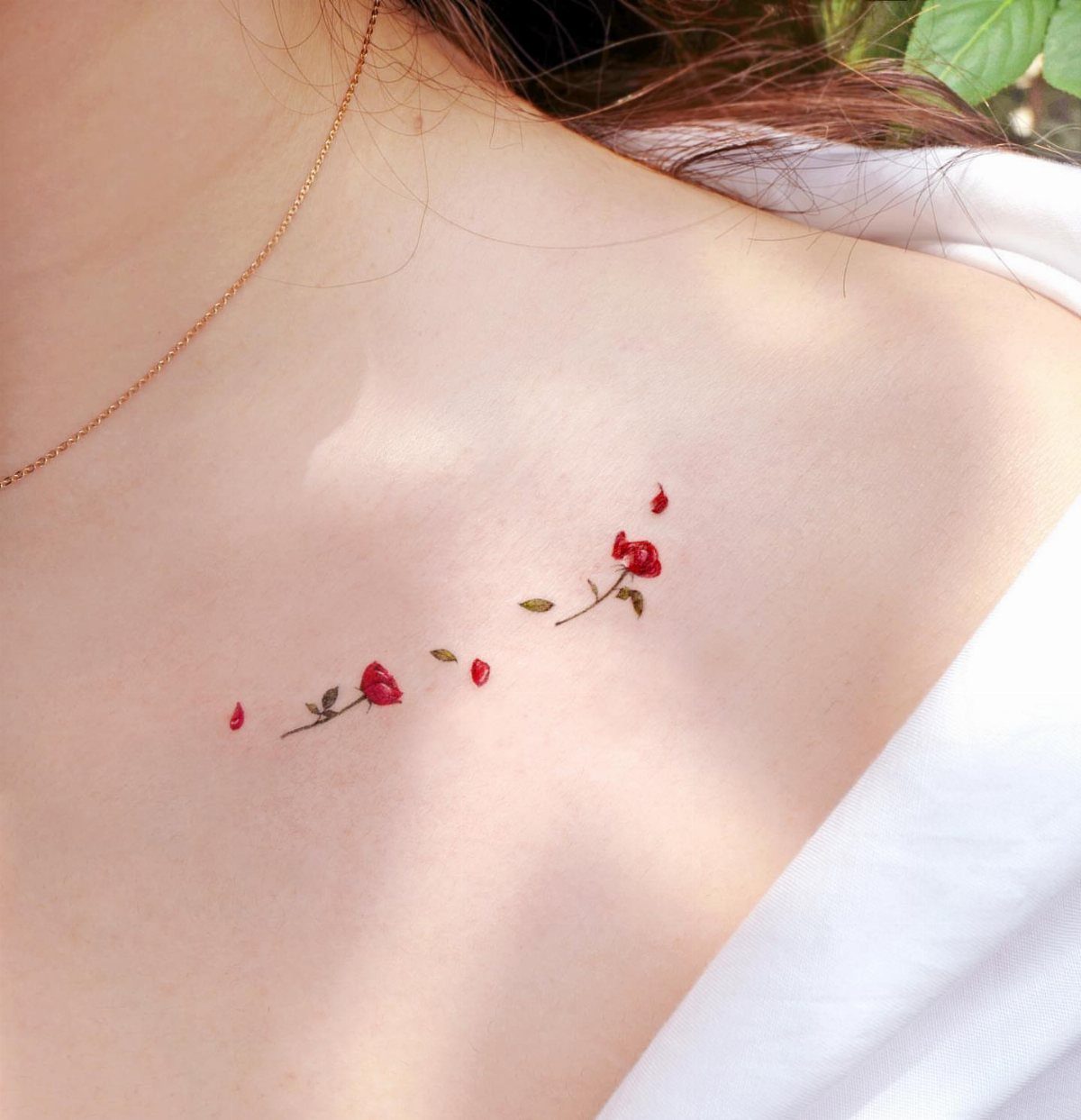 Small red rose tattoos with green leaves along a woman's collarbone.