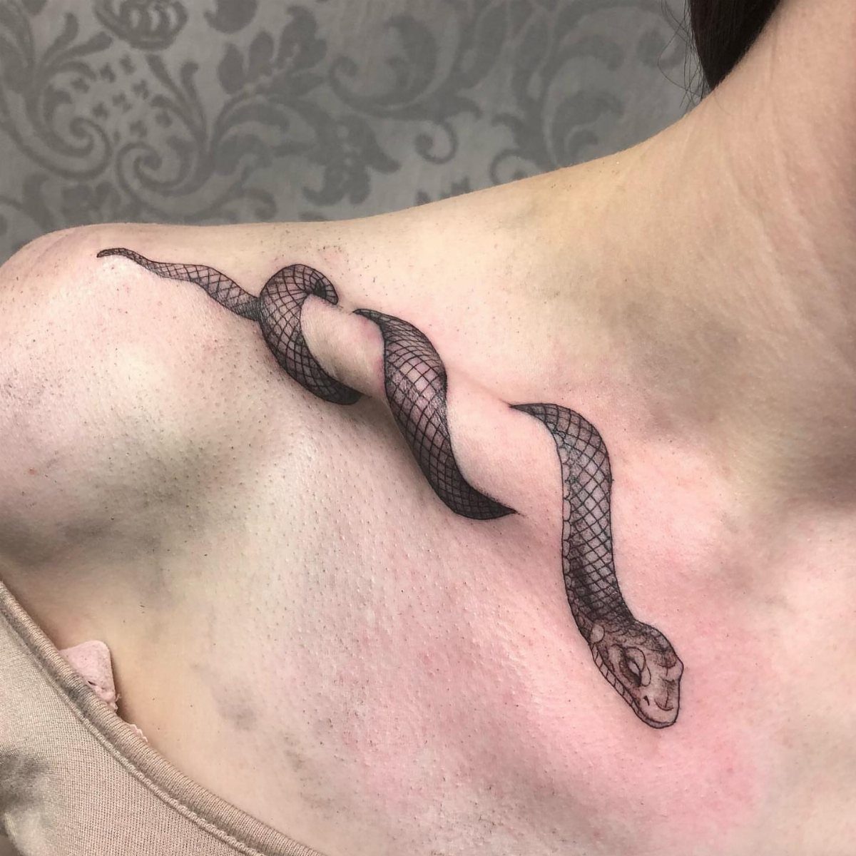 Snake tattoo with detailed scales coiling across a person's collarbone and chest.