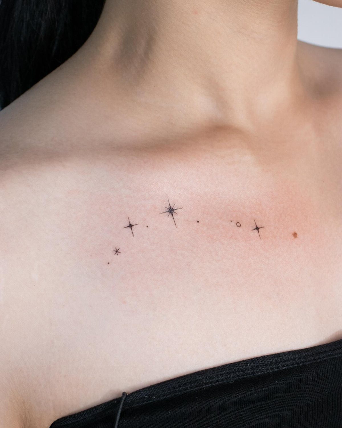 Small black star tattoos along a woman's collarbone in various minimalist styles.