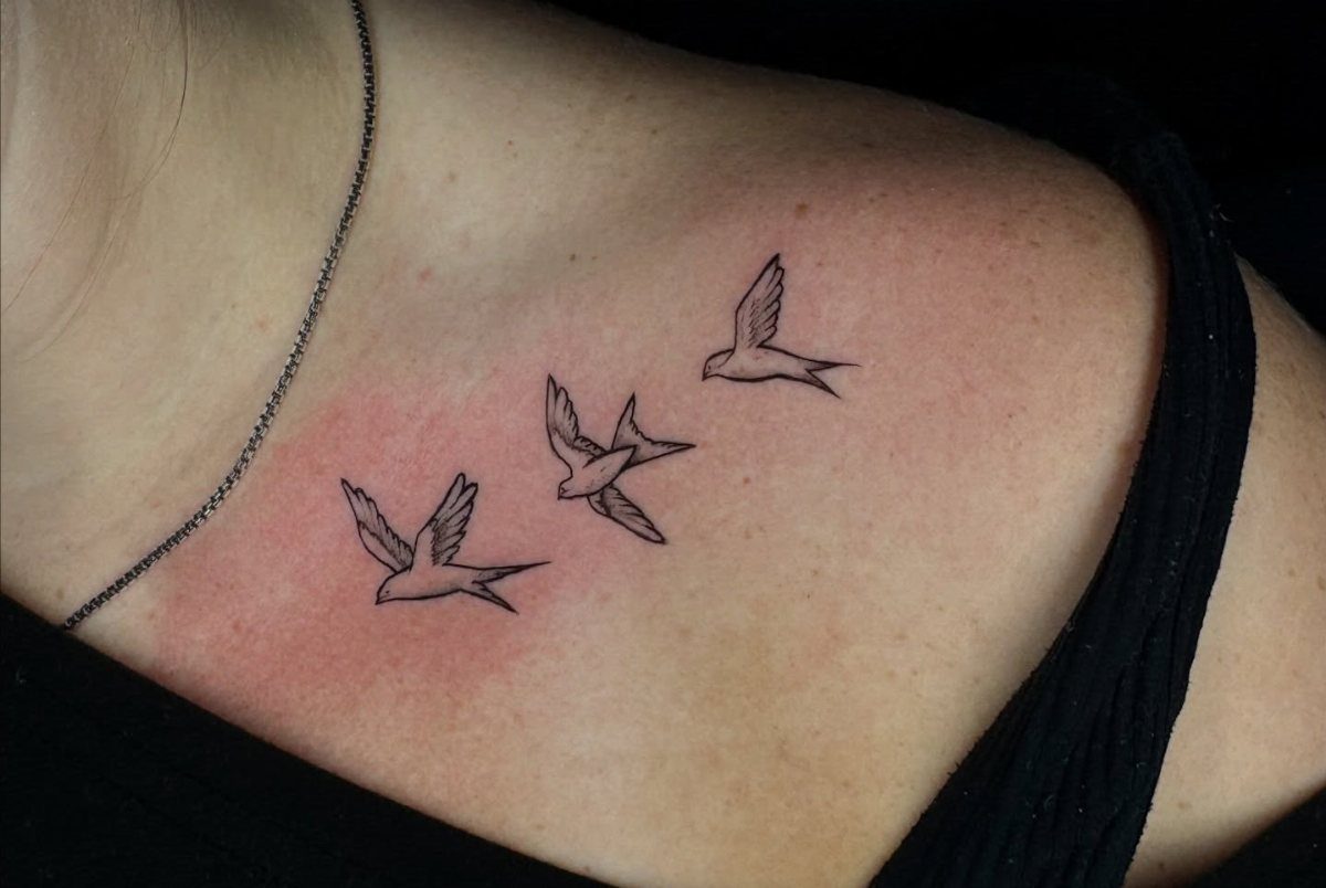 Three small black swallow tattoos in flight along a woman's collarbone.