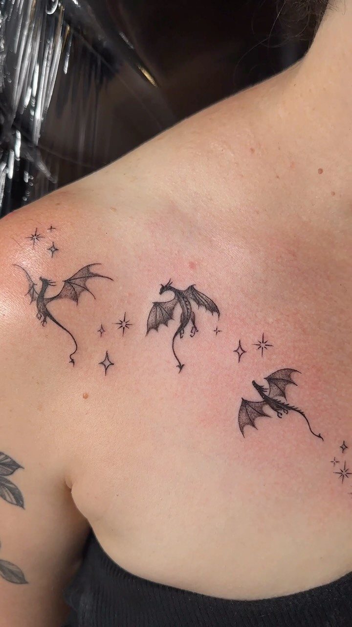 Three small black dragon tattoos with stars on a person's collarbone area.