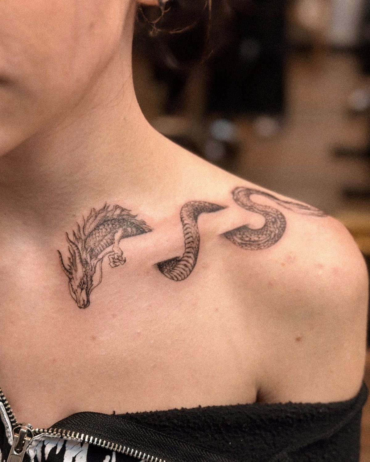 Dragon tattoo in black ink winding across a person's collarbone and shoulder.