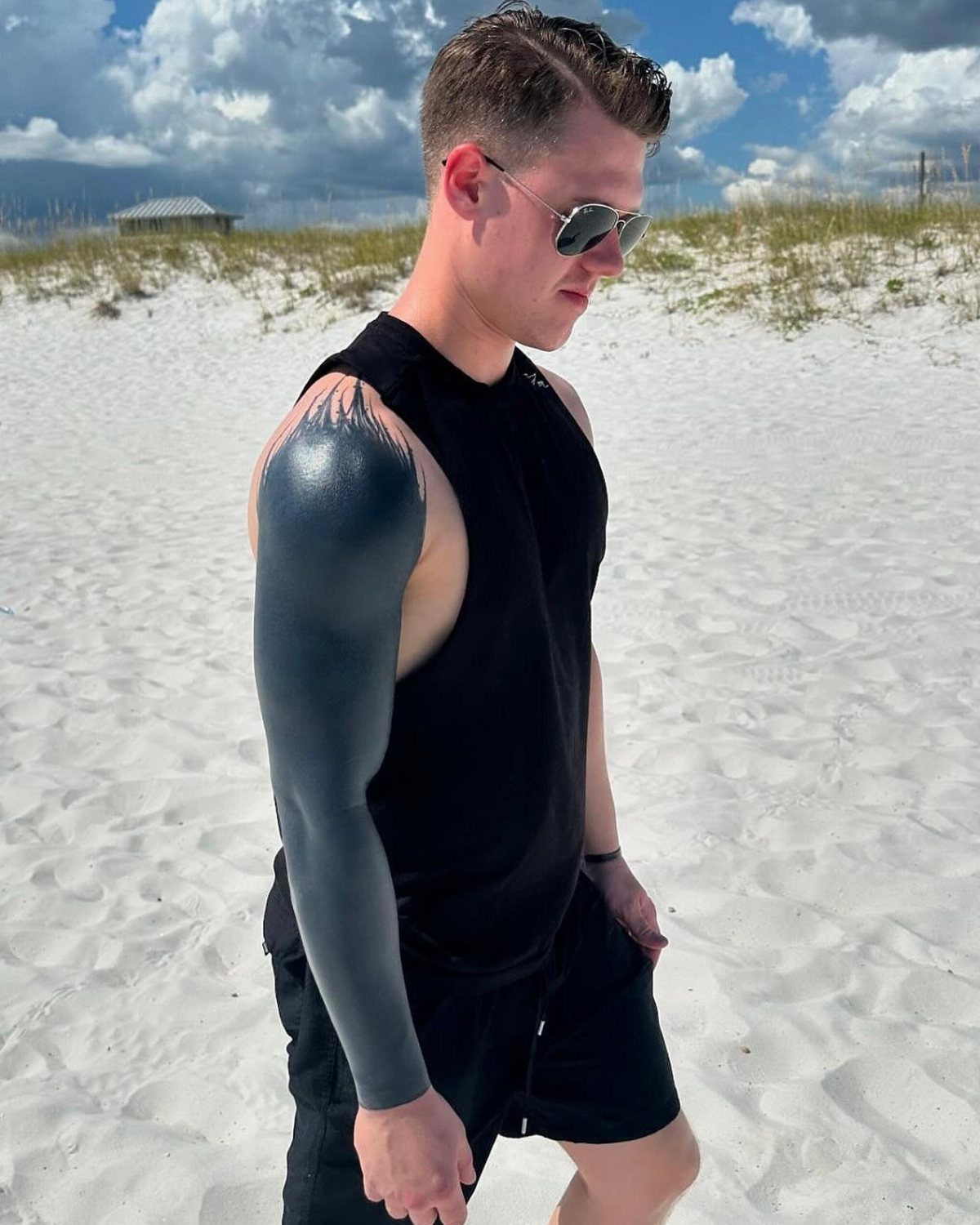 Man on a beach with a solid black blackout tattoo covering his entire arm.