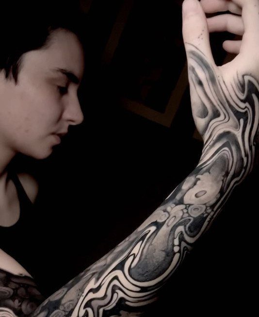 Person with a flowing, organic blackwork tattoo covering their arm and hand.