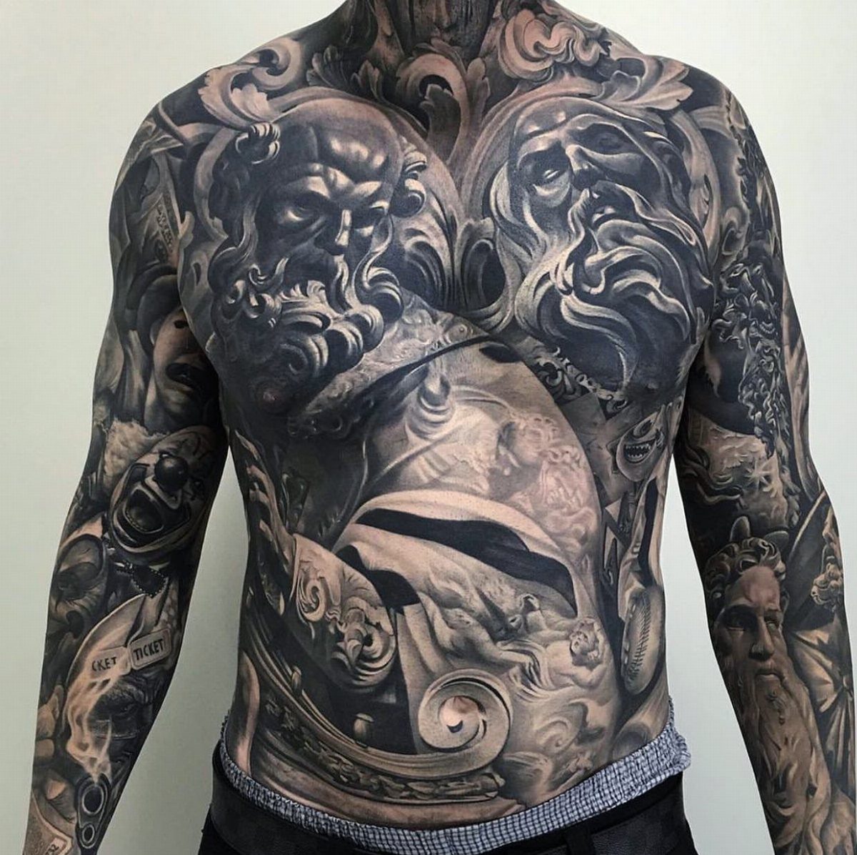 Man's torso and arms covered in detailed black and grey classical sculpture tattoos.