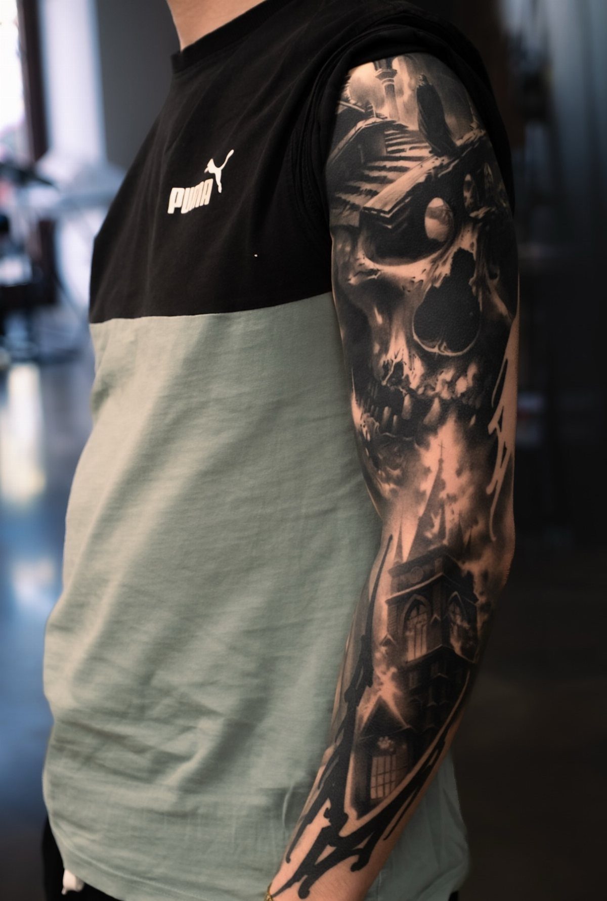 Detailed black and grey tattoo sleeve on a man's arm featuring a skull and gothic building.