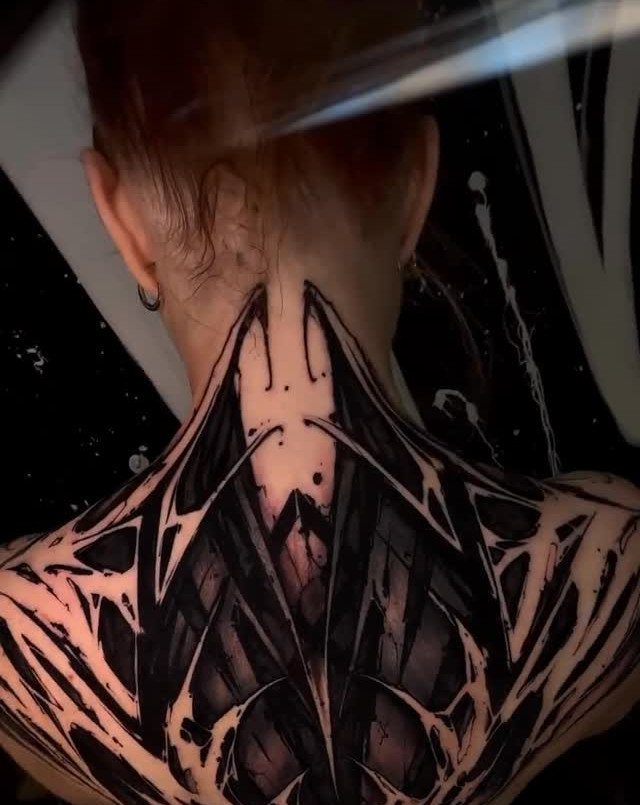 Intricate blackwork tattoo with sharp organic shapes covering a person's upper back and neck.
