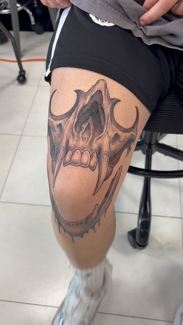 Detailed monster skull tattoo with sharp fangs on a person's knee