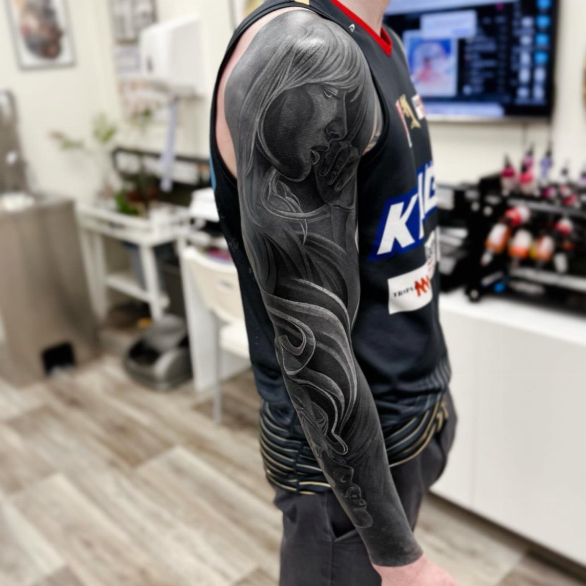 Man's arm with a detailed black and grey ornamental sleeve tattoo.