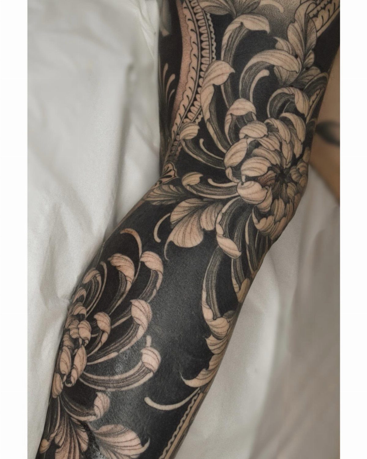 Detailed blackwork tattoo of large floral patterns covering a person's arm.