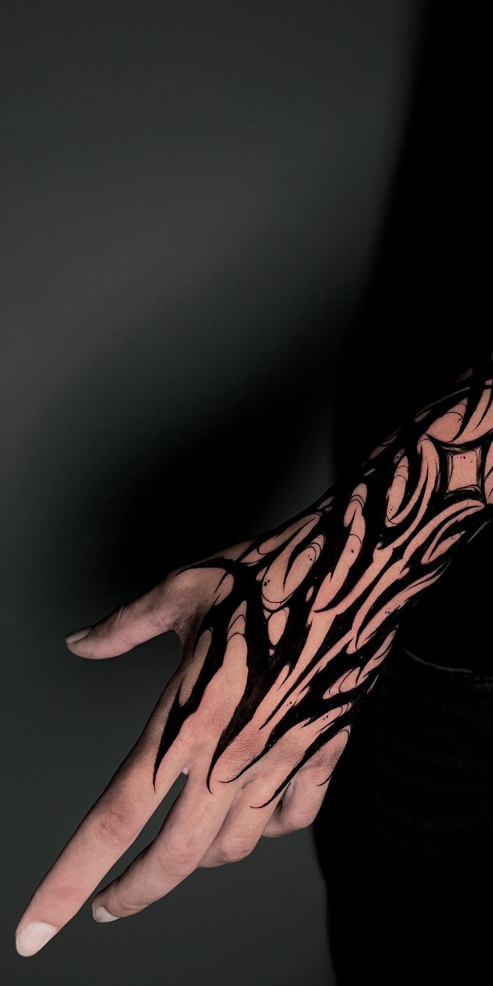 Hand and forearm with bold black tribal blackwork tattoos featuring sharp organic lines