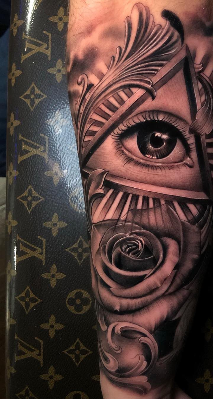 All-seeing eye tattoo inside a triangle with a rose and ornate scrolls.