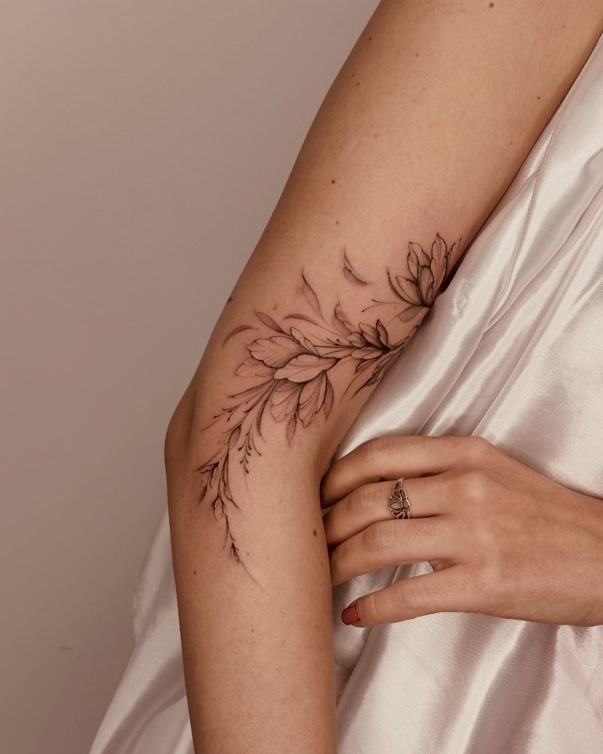 Floral bloom tattoo with leaves wrapping around a person's elbow and upper arm.