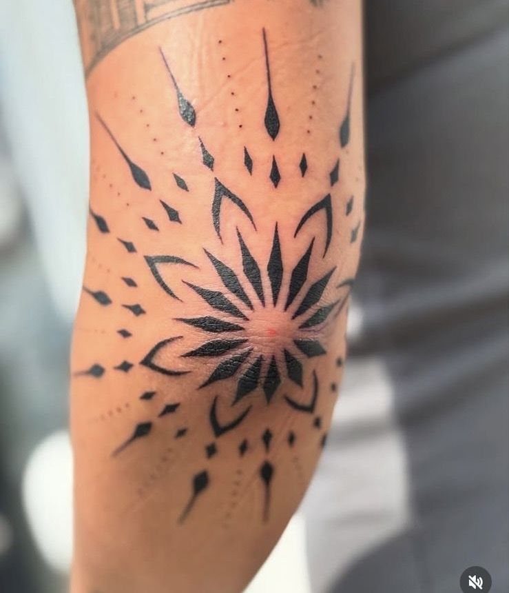 Geometric star tattoo on a person's elbow with radiating black ink lines.
