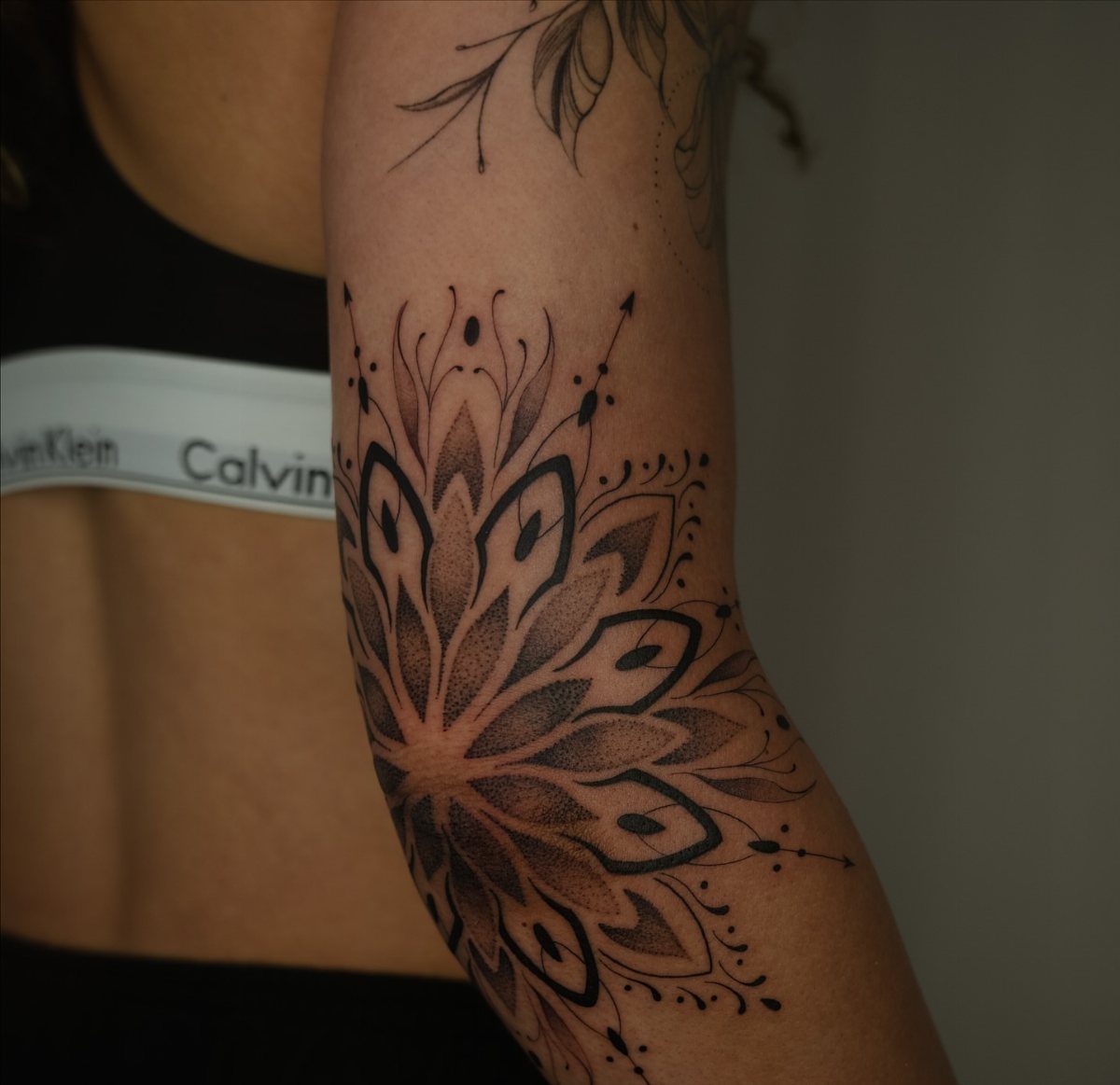 Mandala tattoo on a person's elbow with symmetrical black ink geometric patterns.