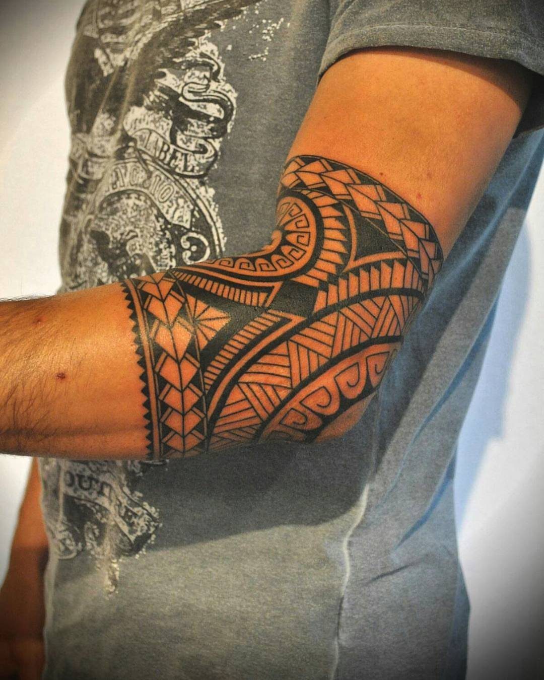 Polynesian tribal tattoo with bold black geometric patterns covering a person's elbow.