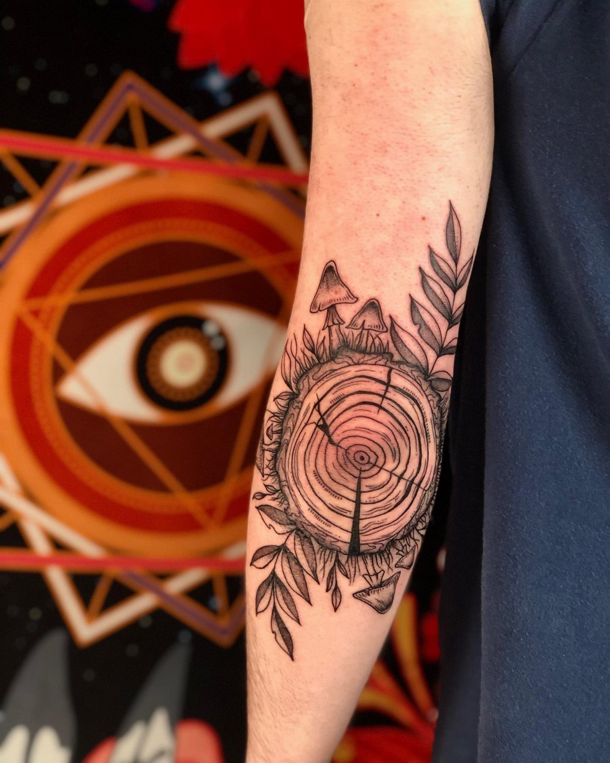 Tree ring tattoo with mushrooms and leaves on a person's forearm.